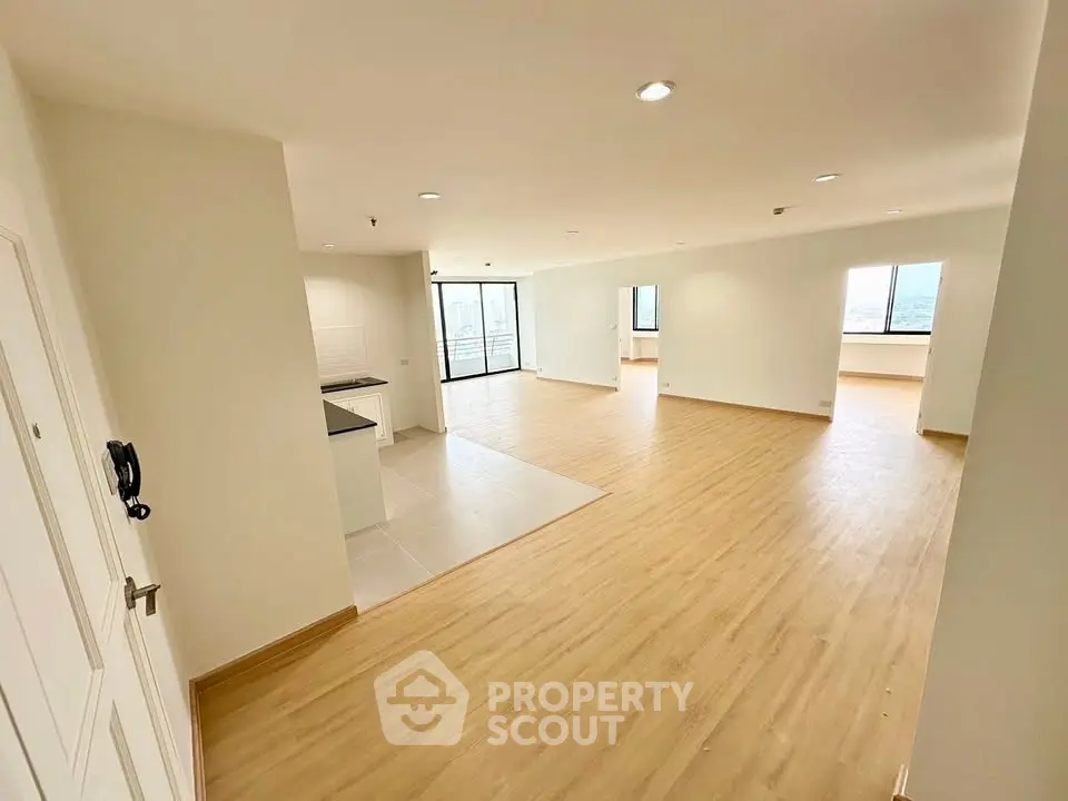 Spacious open-plan living area with wooden flooring and large windows offering natural light.