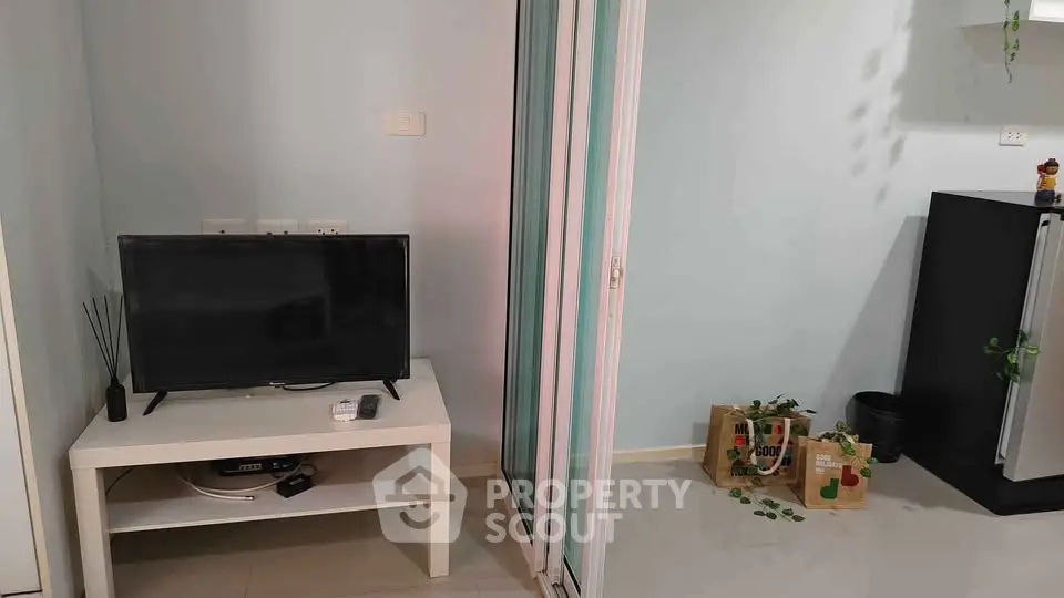Modern living room with TV and sliding glass door leading to a bright space.