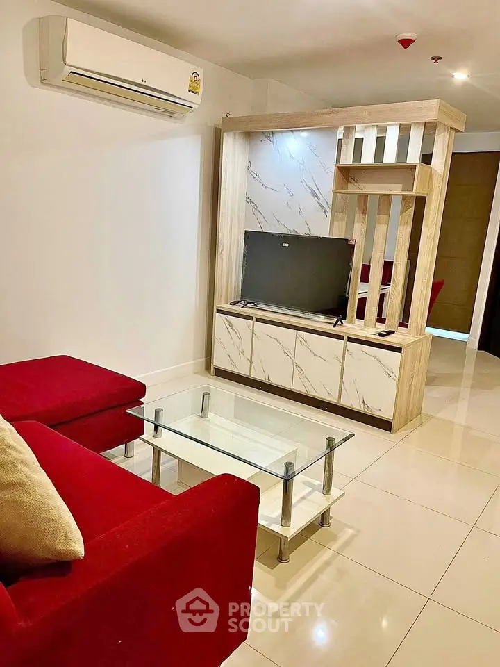 Modern living room with red sofa, glass coffee table, and stylish TV unit in a bright apartment.
