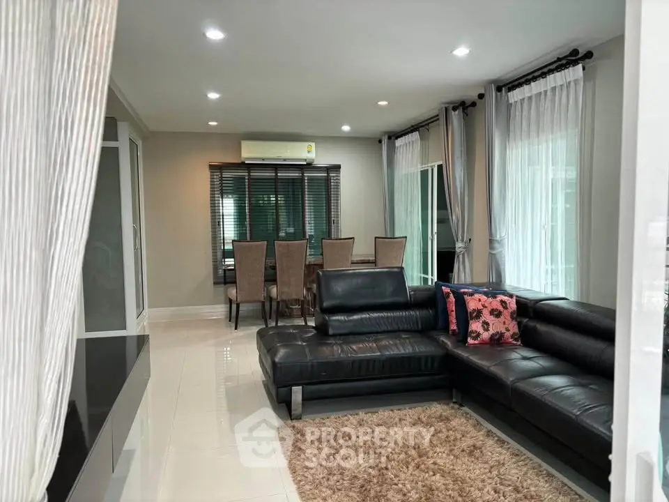 Spacious living room with modern black leather sofa and elegant dining area, perfect for family gatherings.