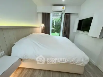 Cozy modern bedroom with large bed, wall-mounted TV, and natural light from window.