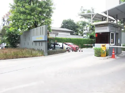 Gated entrance of a modern residential complex with security booth and lush greenery.