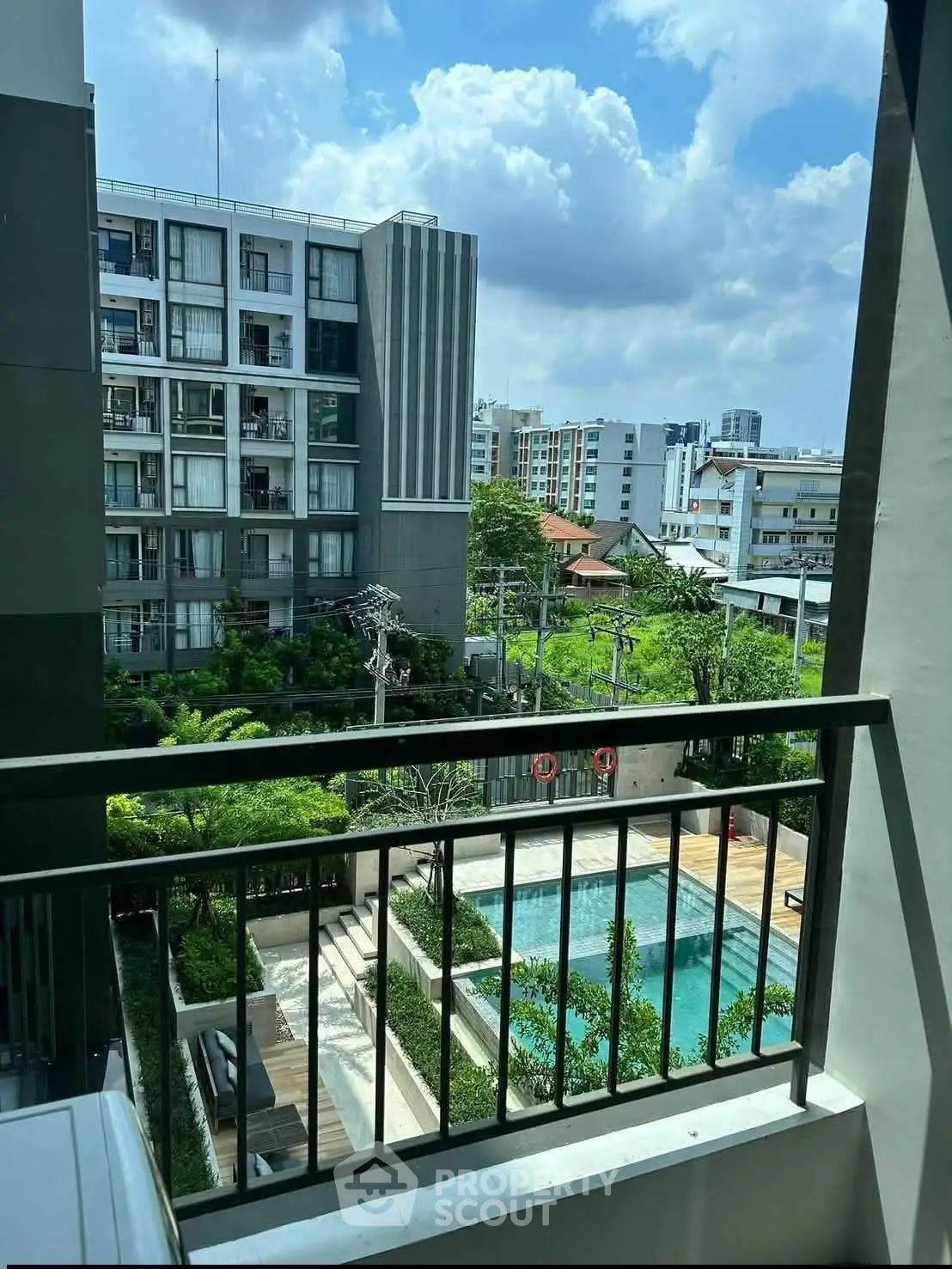 Modern apartment balcony view overlooking pool and lush garden in urban setting.