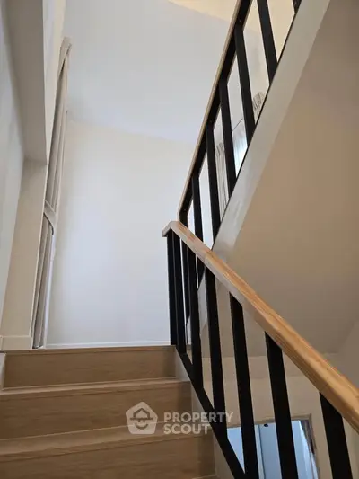 Modern staircase with sleek wooden handrail and black balusters in a bright interior.