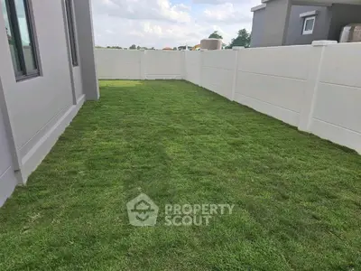Spacious backyard with lush green lawn and privacy fence in modern residential area.