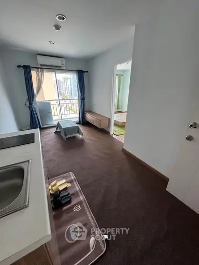 Modern apartment interior with compact kitchen and cozy living area, featuring a small balcony with city views.