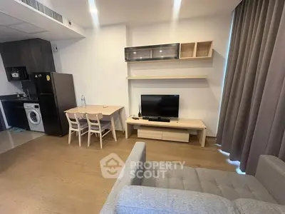 Modern living room with open kitchen, featuring sleek furniture and appliances.