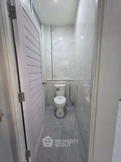 Compact modern bathroom with sleek marble tiles and white fixtures.