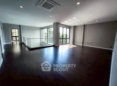 Spacious modern living room with dark wood flooring and large windows offering natural light.