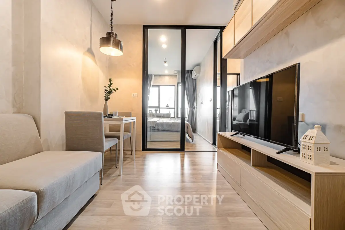 Modern living room with sleek design and glass partition leading to bedroom, featuring cozy seating and stylish decor.