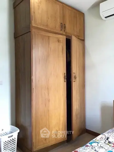 Spacious wooden wardrobe in a cozy bedroom with air conditioning, perfect for organized living.