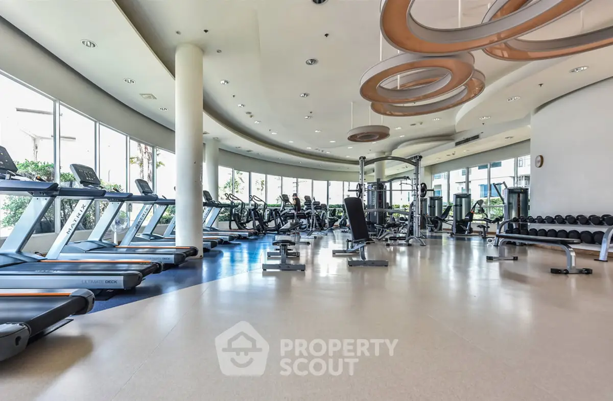 Spacious modern gym with state-of-the-art equipment and large windows offering natural light.