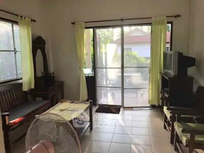 Charming living room with natural light and garden view, featuring traditional wooden furniture and sliding glass doors.