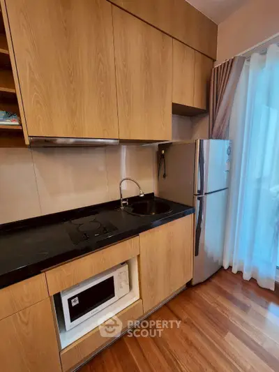 Modern kitchen with wooden cabinets, microwave, and fridge in a cozy apartment setting.