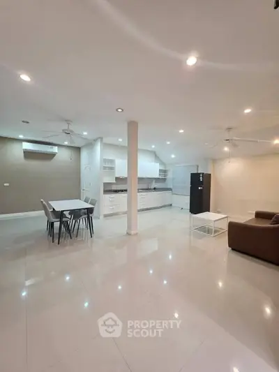 Spacious open-plan living room with modern kitchen and dining area, featuring sleek design and ample lighting.