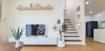 Modern living room with stylish decor and staircase, featuring a sleek TV setup and elegant plants.