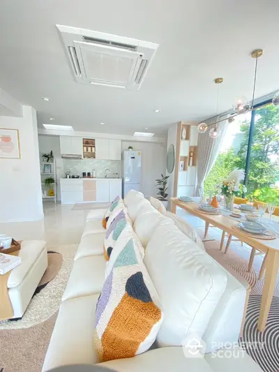 Spacious open-plan living room with modern kitchen and dining area, featuring large windows and stylish decor.