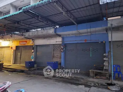 Street view of closed commercial units with metal shutters in urban area.