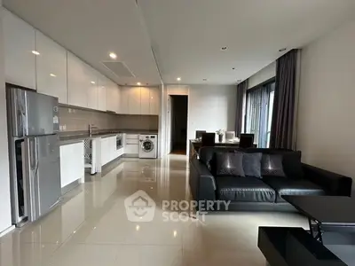 Modern open-plan living room with sleek kitchen, black sofa, and dining area in a stylish apartment.