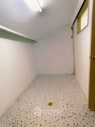 Compact storage room with terrazzo flooring and minimal lighting, ideal for organizing household items.