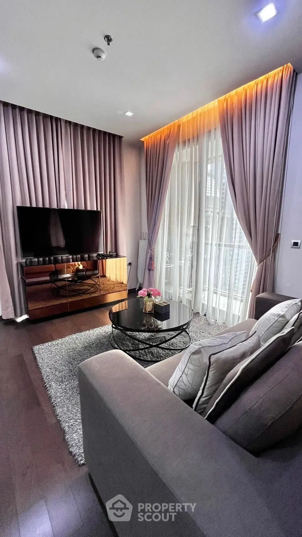 Elegant living room with plush sofa, modern TV setup, and floor-to-ceiling curtains.