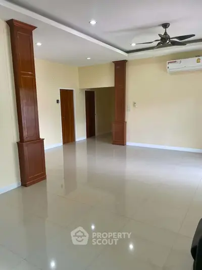 Spacious living room with modern ceiling fan and air conditioning, featuring elegant wooden columns and glossy tiled floor.