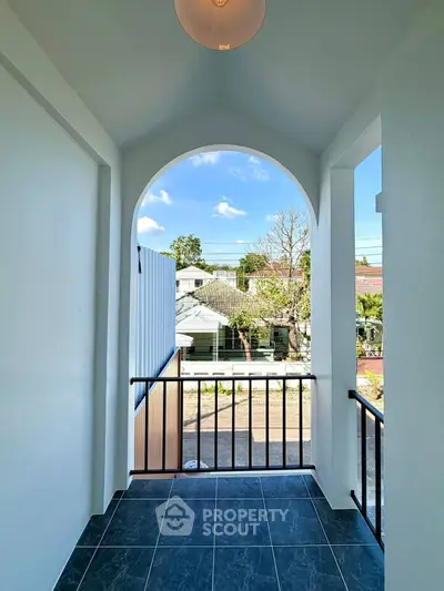 Charming balcony with archway offering a picturesque view of suburban homes and blue skies.