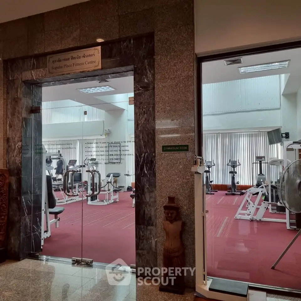 Spacious fitness center with modern gym equipment and red carpet flooring.