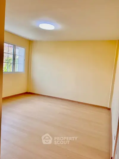 Spacious empty room with wooden flooring and natural light from window