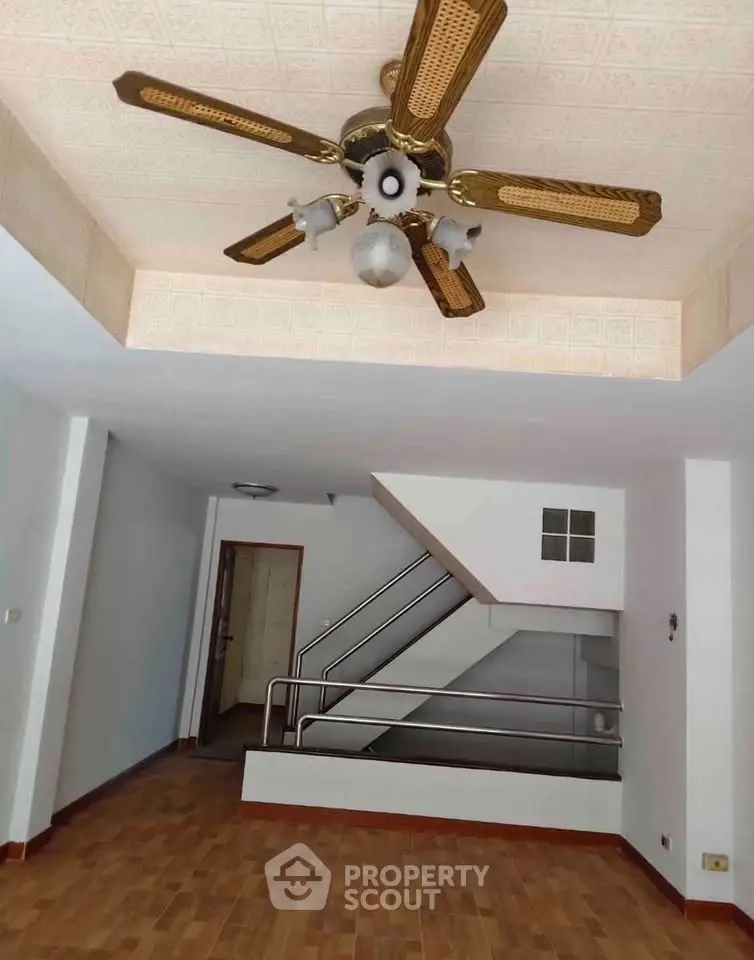 Spacious living room with wooden flooring and ceiling fan, featuring a modern staircase.