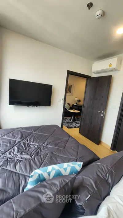 Modern bedroom with wall-mounted TV and air conditioning, featuring stylish bedding and wooden flooring.