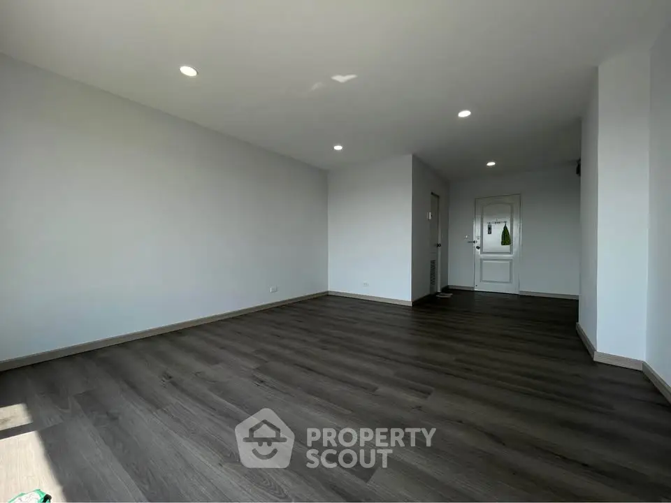 Spacious empty living room with modern dark wood flooring and recessed lighting.