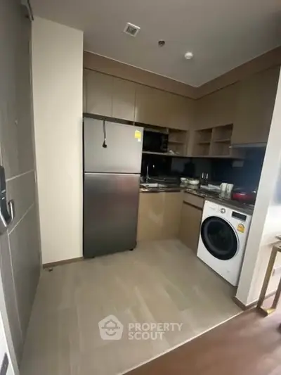 Modern kitchen with stainless steel appliances and washing machine in compact layout.