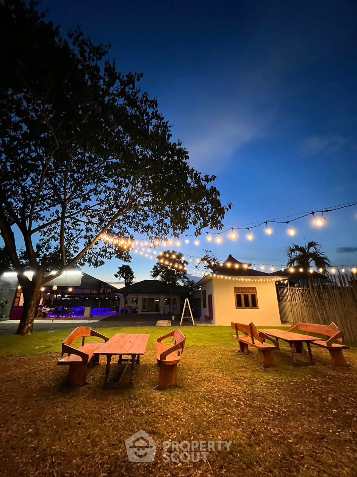 Charming outdoor garden with string lights and wooden seating, perfect for evening gatherings.