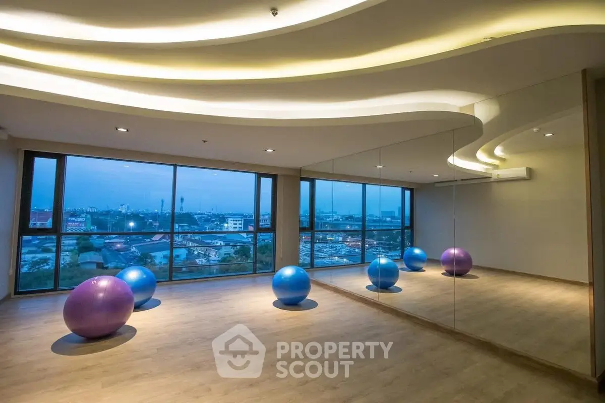 Spacious gym with mirrored walls and vibrant exercise balls offering a panoramic city view.