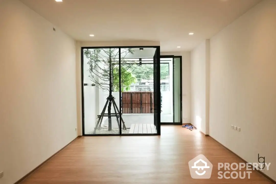 Spacious and bright living room with large glass doors opening to a serene balcony, offering a seamless indoor-outdoor living experience.