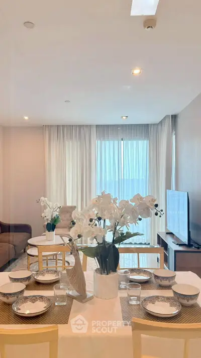 Elegant living room with dining area, modern decor, and large windows offering natural light.