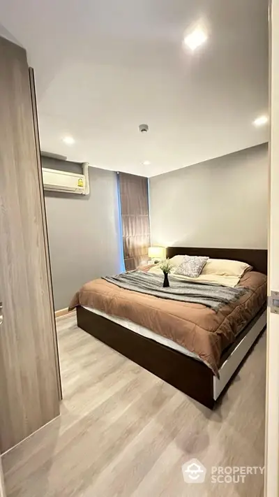 Modern bedroom with cozy decor and natural light, featuring sleek wooden flooring and neutral tones.