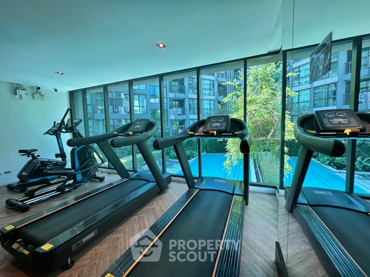 Modern gym with treadmills overlooking a pool and lush greenery in a luxury apartment complex.