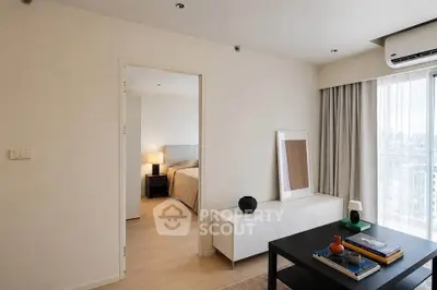 Modern living room with sleek furniture and a view into a cozy bedroom, featuring natural light and stylish decor.