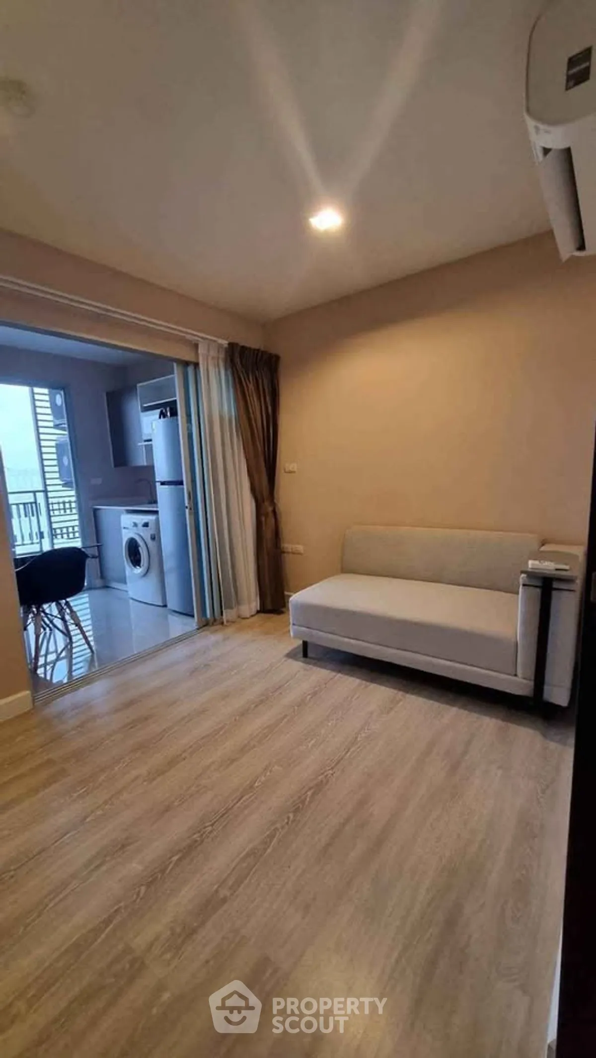 Modern living room with open kitchen and balcony view, featuring sleek furniture and wooden flooring.