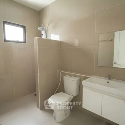 Modern bathroom with sleek design and neutral tiles, featuring a shower and vanity unit.