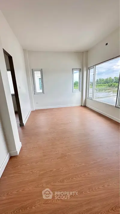 Spacious empty room with large windows and wooden flooring, offering abundant natural light and scenic views.