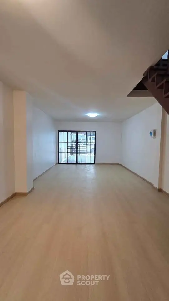 Spacious empty room with wooden flooring and large window for natural light.