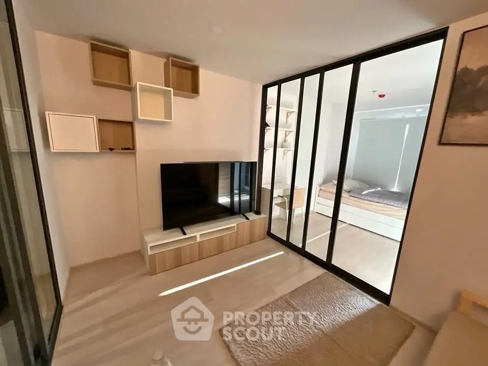 Modern living room with sliding glass doors leading to a cozy bedroom, featuring stylish shelving and a sleek TV unit.