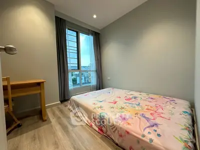 Cozy bedroom with large window and wooden flooring, featuring a charming bedspread.