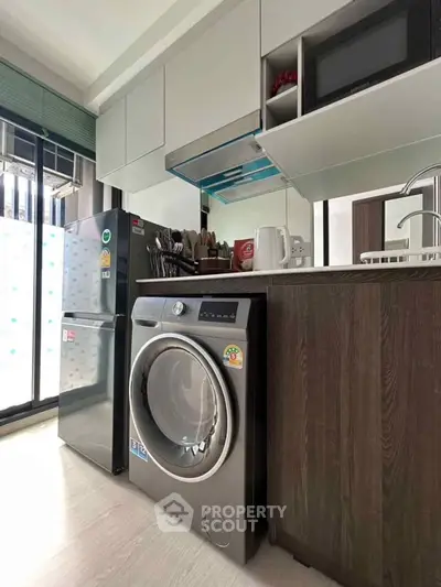 Modern kitchen with sleek appliances including washing machine and fridge, featuring stylish cabinetry and open layout.