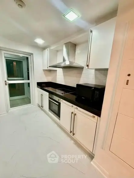 Modern kitchen with sleek white cabinets and black countertops, featuring built-in appliances and stylish lighting.