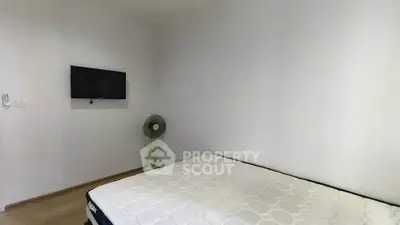 Minimalist bedroom with wall-mounted TV and fan, featuring a simple bed setup.