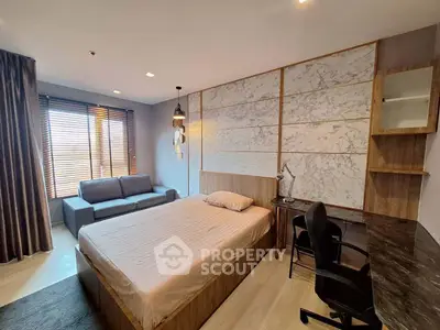 Modern bedroom with stylish decor, featuring a cozy bed, sofa, and workspace with natural light.